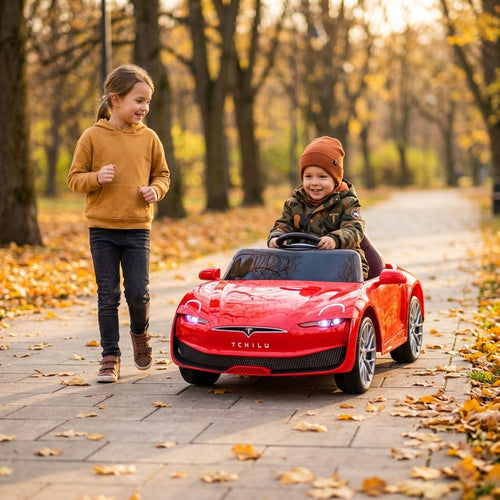Auto na akumulator crvene boje koji dečak vozi u parku dok ga prati sestra